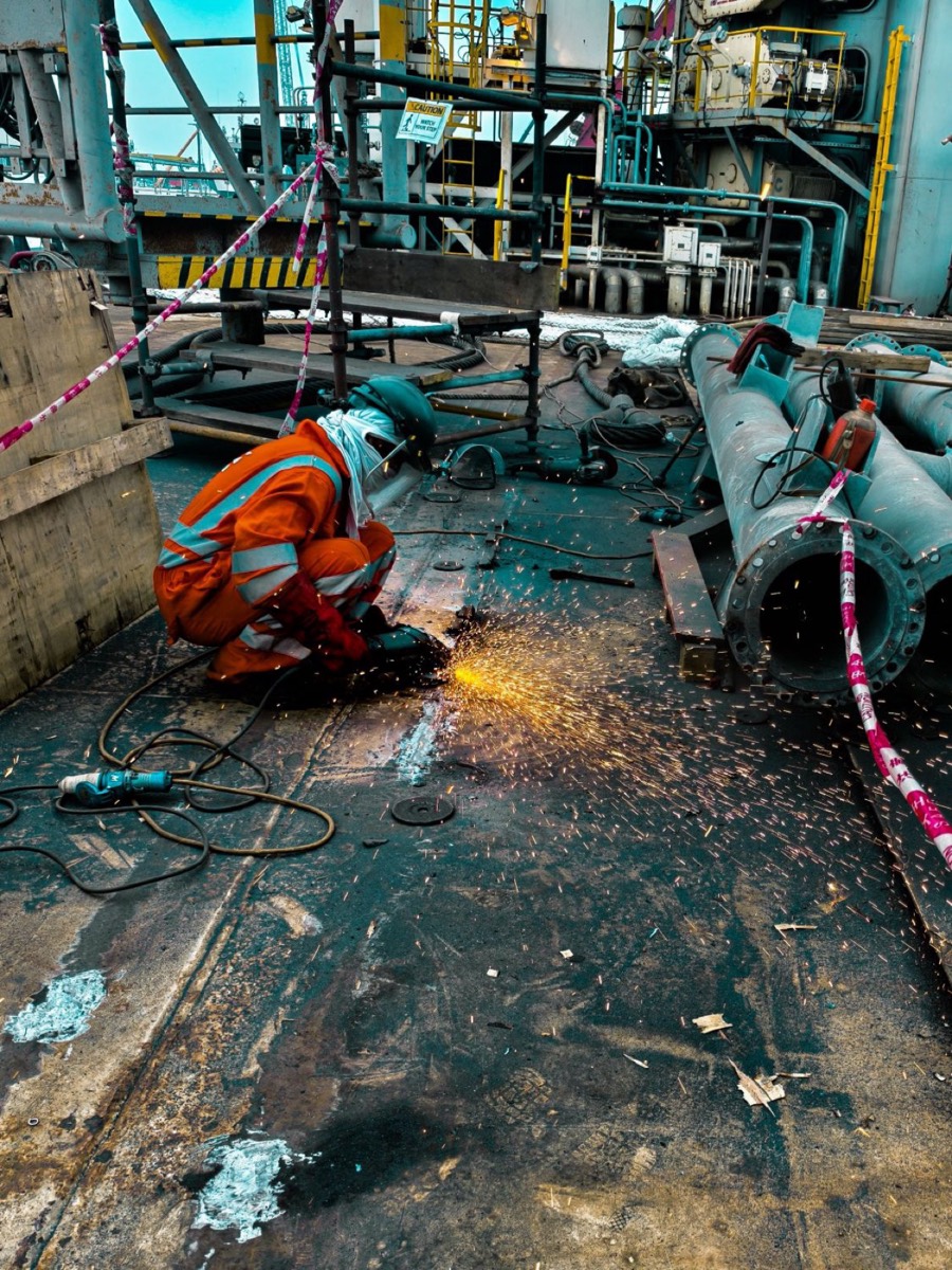 Worker in orange coveralls grinding metal on an industrial platform